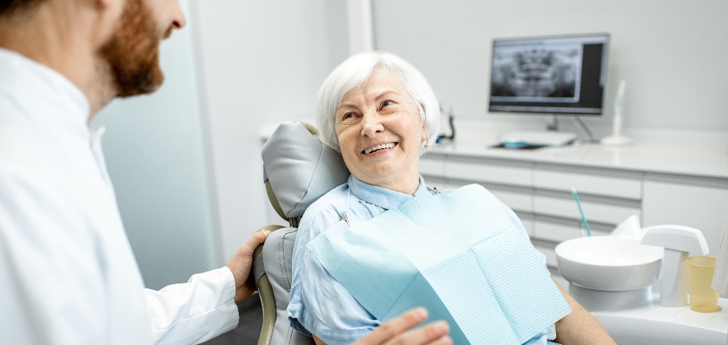 Beautiful elder woman with healthy smile sitting during the consultation with dentist at the dental office