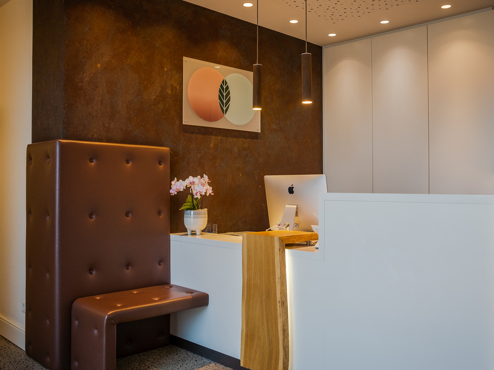 Empfangsbereich mit braunem Sitz, Orchidee, Holz-Akzent und Wandkunst in neutralen Farbtönen.