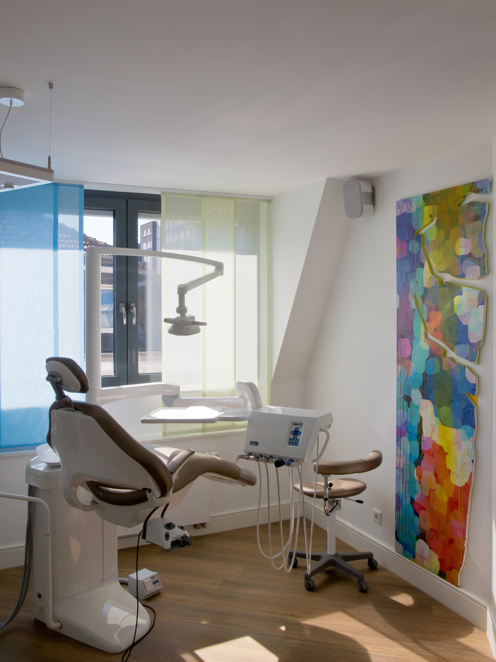 Zahnarztpraxis mit bunter Kunst an der Wand, helle Fenster, moderner Zahnarztstuhl.