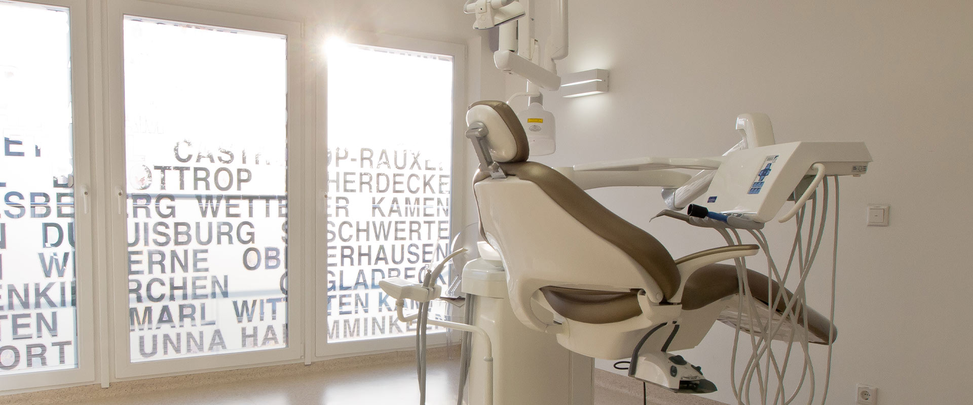 Zahnarztstuhl in modernem Praxisraum mit hellen Wänden; Blick auf große Fenster und stilvolle Möbel.