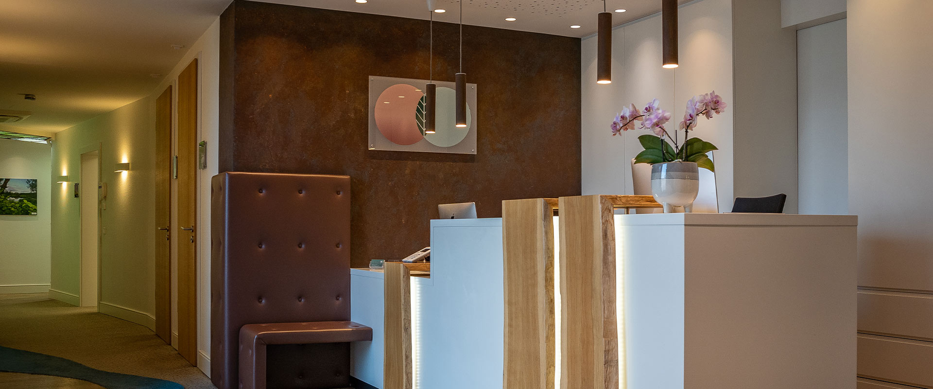 Moderne Rezeption mit Holzdetails, brauner Akzentwand, Orchidee und Kunstwerk in warmen Farben.