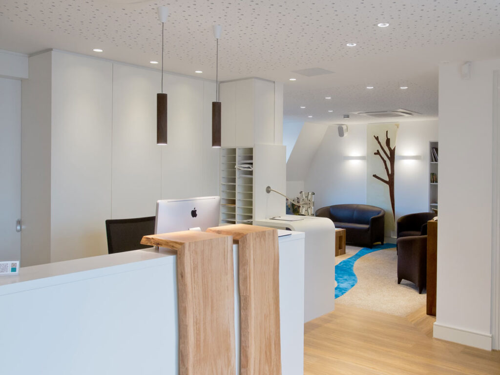 Helles, modernes Büro mit Empfangstresen aus Holz, Ledersesseln und blauem Teppich.